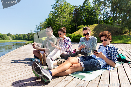 Image of friends with smartphone on lake pier in summer