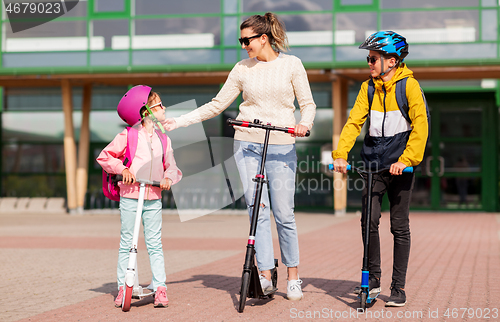 Image of happy school children with mother riding scooters