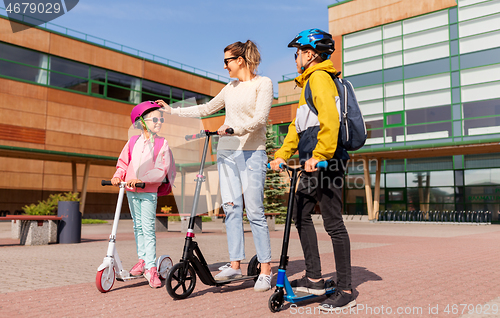 Image of happy school children with mother riding scooters