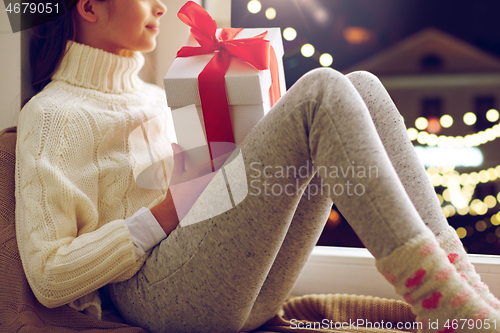 Image of girl with christmas gift sitting on window sill