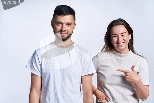 Image of Smiling couple standing over light background, joyful female pointing at guy and winking