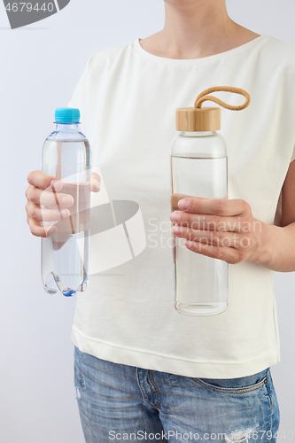 Image of The woman holds two bottles of glass and plastic of clean fresh water.