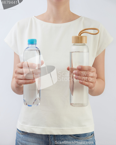 Image of Two bottles of glass and plastic of clean fresh water in a woman\'s hands.