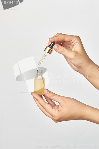 Image of Bottle and pipet of medical cannabis CBD oil in hands against a light grey background.