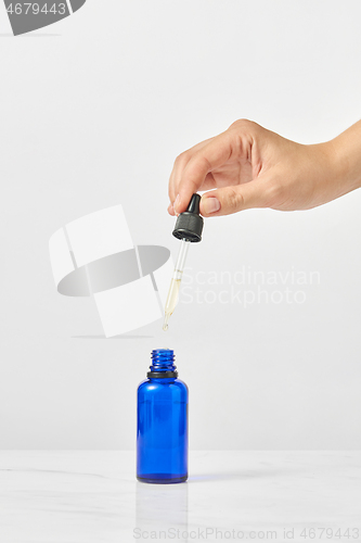 Image of Woman\'s hand holds pipet of natural extract CBD oil against a light grey background