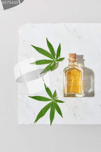 Image of Medical marijuana oil and green cannabis leaves on a light grey marble background.