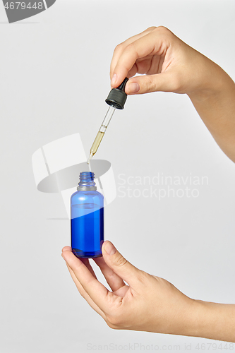 Image of Female\'s hand holds a pipet of natural extract CBD oil against a light grey background.