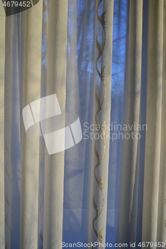 Image of translucent curtains behind which the sky and trees