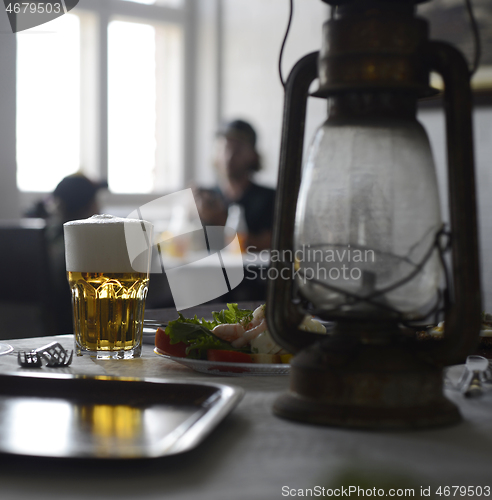 Image of glass of beer and shrimp salad on a table with a kerosene lamp