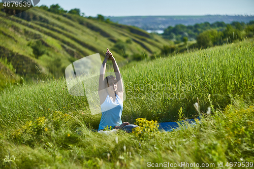 Image of Young woman doing yoga in green summer meadow