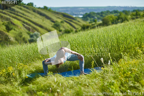 Image of Young woman doing yoga in green summer meadow