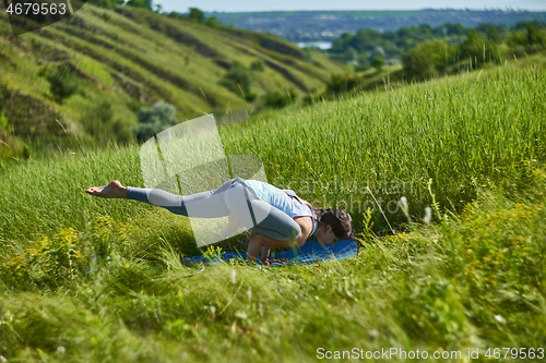 Image of Young woman doing yoga in green summer meadow