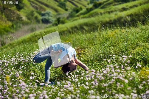 Image of Young woman doing yoga in green summer meadow