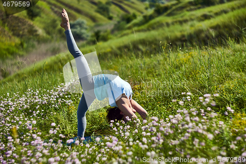 Image of Young woman doing yoga in green summer meadow