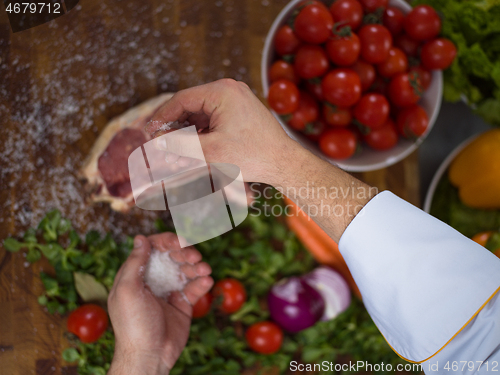 Image of Chef putting salt on juicy slice of raw steak