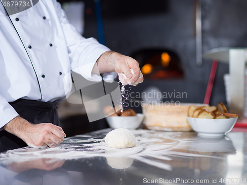 Image of chef sprinkling flour over fresh pizza dough