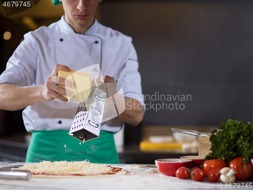 Image of chef sprinkling cheese over fresh pizza dough