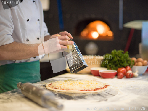 Image of chef sprinkling cheese over fresh pizza dough