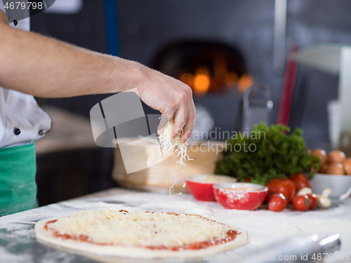 Image of chef sprinkling cheese over fresh pizza dough