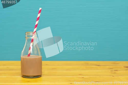 Image of Glass bottle half full with chocolate milkshake with paper straw