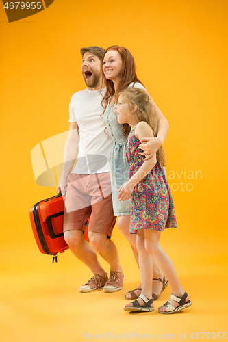 Image of Happy parents with daughter and suitcase at studio isolated on yellow background