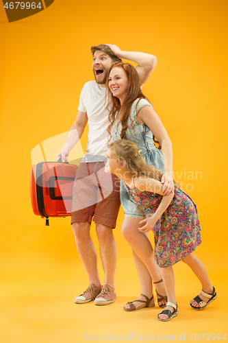 Image of Happy parents with daughter and suitcase at studio isolated on yellow background