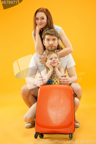 Image of Happy parents with daughter and suitcase at studio isolated on yellow background