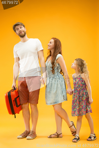 Image of Happy parent with daughter and suitcase at studio isolated on yellow background