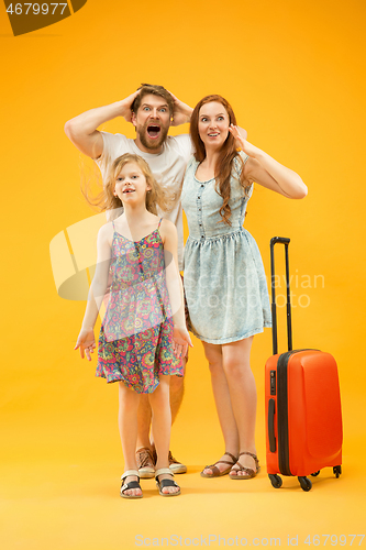 Image of Happy parents with daughter and suitcase at studio isolated on yellow background