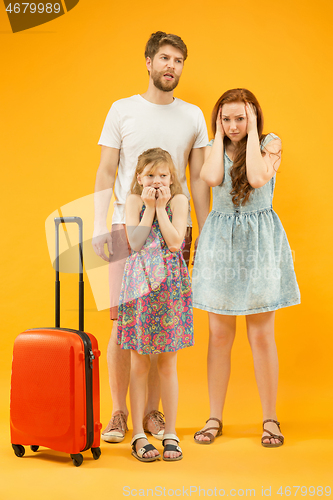 Image of Sad parents with daughter and suitcase at studio isolated on yellow background