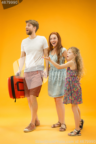 Image of Happy parents with daughter and suitcase at studio isolated on yellow background