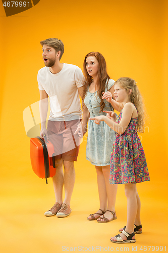 Image of Sad parents with daughter and suitcase at studio isolated on yellow background