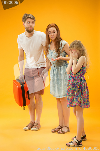 Image of Sad parents with daughter and suitcase at studio isolated on yellow background