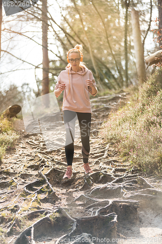 Image of Active sporty woman listening to the music while running in autumn fall forest. Female runner training outdoor. Healthy lifestyle image of young caucasian woman jogging outside