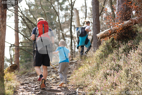 Image of Rear view of unrecognizable young active family hiking together on mountain forest trackin in fall. Parents wearing backpacks and child toys.