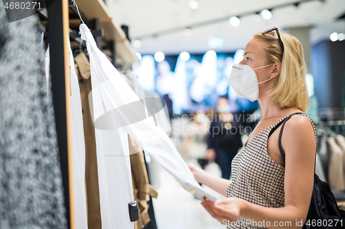 Image of Fashionable woman wearing protective face mask shopping clothes in reopen retail shopping store. New normal lifestyle during corona virus pandemic