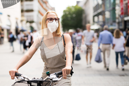 Image of Woman riding bicycle on city street wearing medical face mask in public to prevent spreading of corona virus. New normal during covid epidemic.