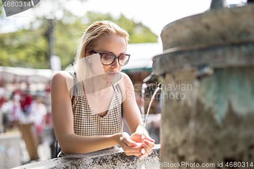 Image of Thirsty young casual cucasian woman drinking water from public city fountain on a hot summer day