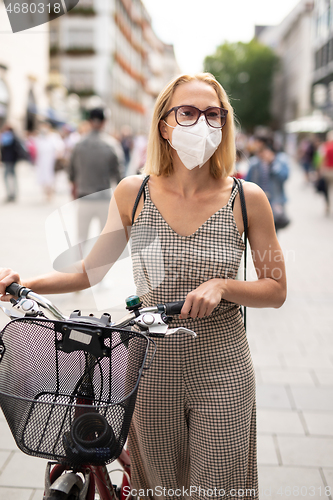 Image of Woman walking by her bicycle on pedestrian city street wearing medical face mask in public to prevent spreading of corona virus. New normal during covid epidemic.