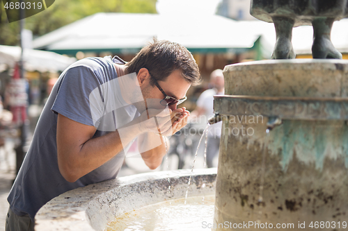 Image of Thirsty young casual cucasian man drinking water from public city fountain on a hot summer day