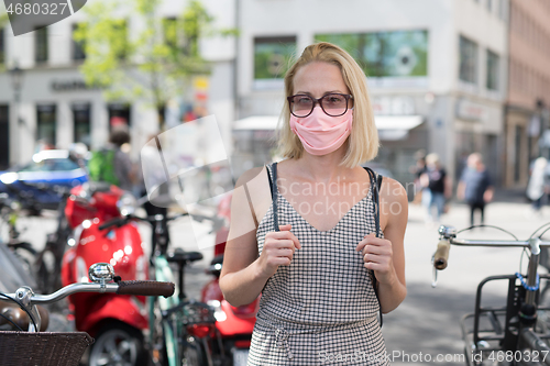 Image of Portrait of casual yound woman walking on the street wearing protective mask as protection against covid-19 virus. Incidental people on the background