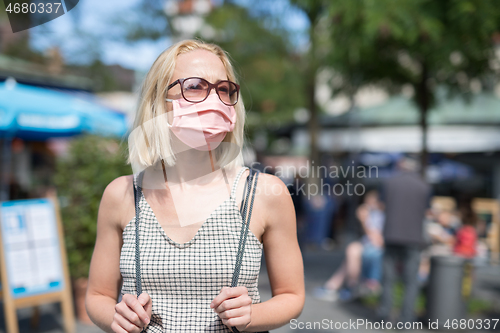 Image of Portrait of casual yound woman walking on the street wearing protective mask as protection against covid-19 virus. Incidental people on the background