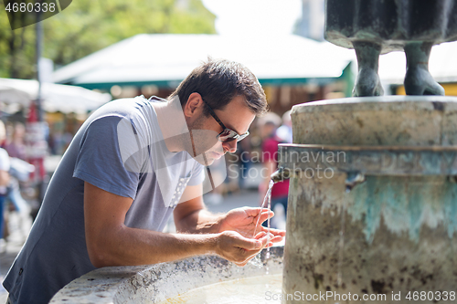 Image of Thirsty young casual cucasian man drinking water from public city fountain on a hot summer day