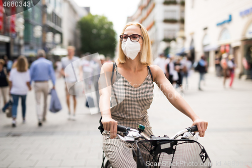 Image of Woman riding bicycle on city street wearing medical face mask in public to prevent spreading of corona virus. New normal during covid epidemic.