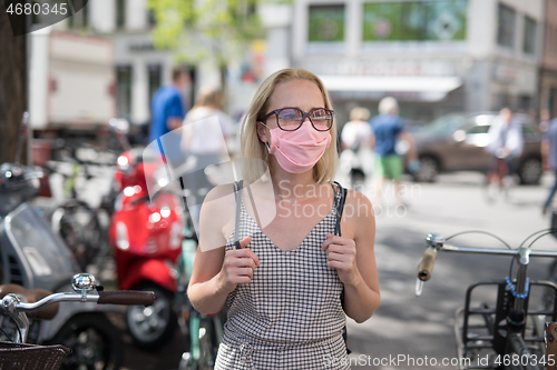Image of Portrait of casual yound woman walking on the street wearing protective mask as protection against covid-19 virus. Incidental people on the background