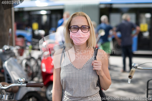 Image of Portrait of casual yound woman walking on the street wearing protective mask as protection against covid-19 virus. Incidental people on the background