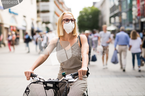 Image of Woman riding bicycle on city street wearing medical face mask in public to prevent spreading of corona virus. New normal during covid epidemic.