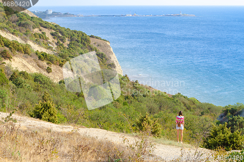 Image of A girl stands on a hill and looks into the distance at the sea