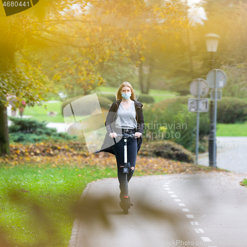 Image of Casual caucasian teenager wearing protective face mask riding urban electric scooter in city park during covid pandemic. Urban mobility concept