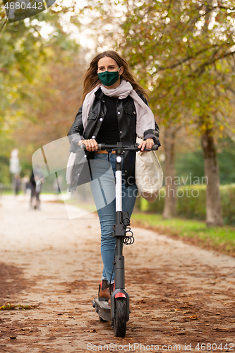 Image of Casual caucasian teenager wearing protective face mask riding urban electric scooter in city park during covid pandemic. Urban mobility concept